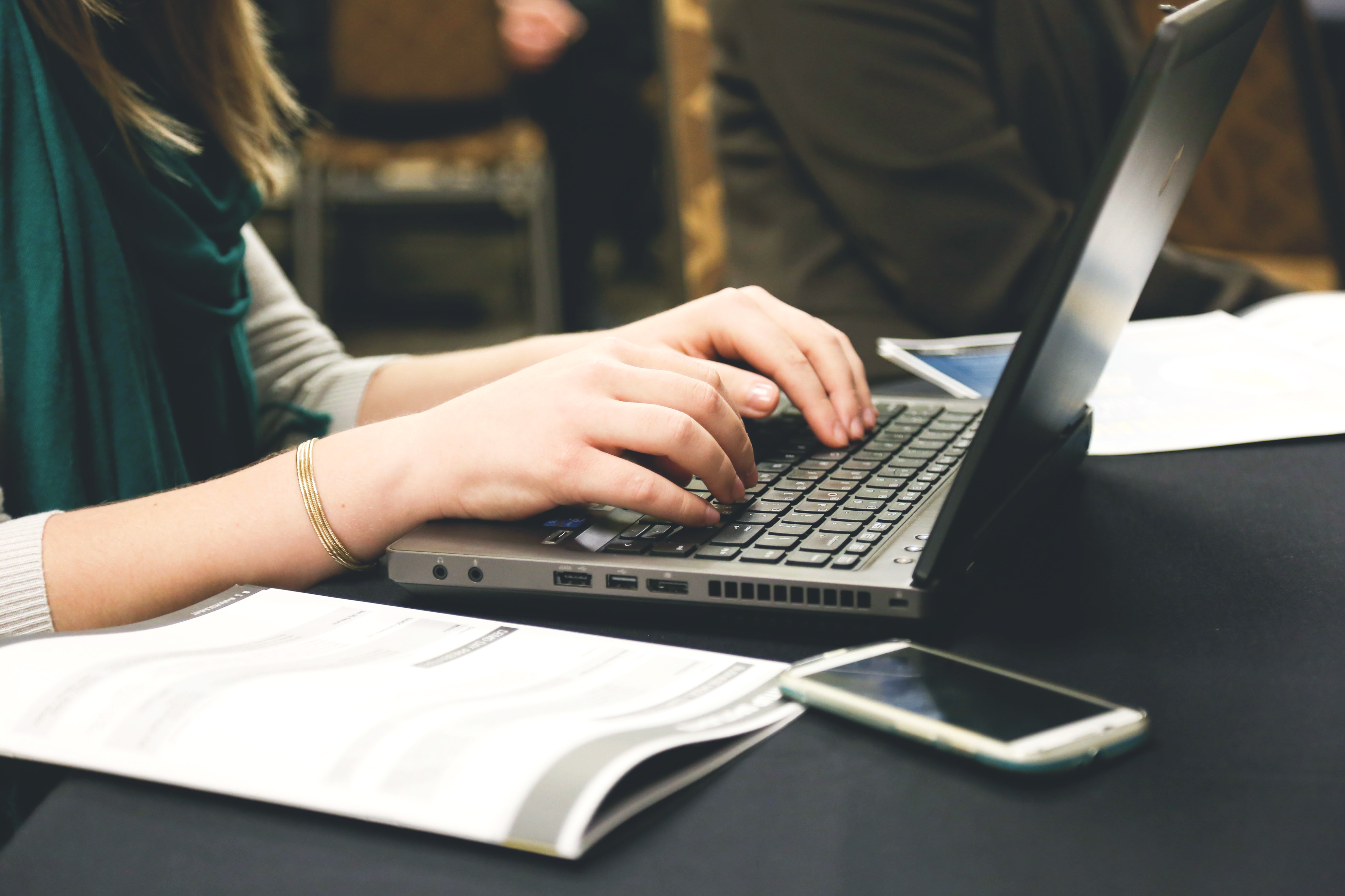 close-up shot of a woman typing on her laptop with a notebook next to her