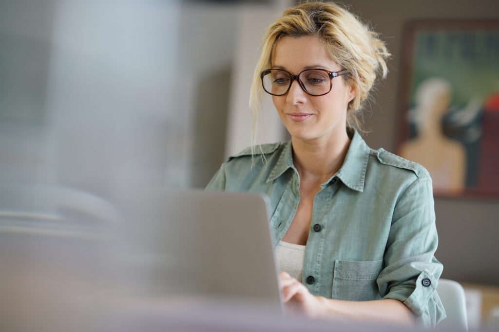 woman with eyeglasses smilingly typing on her laptop