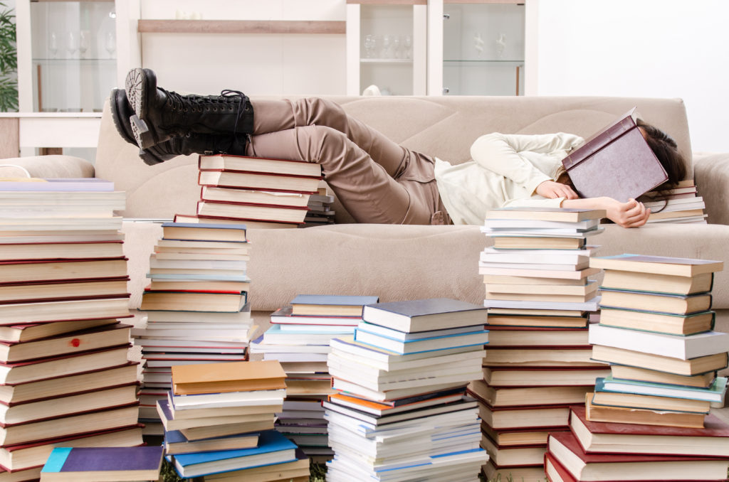 woman asleep on the couch next to a giant pile of books