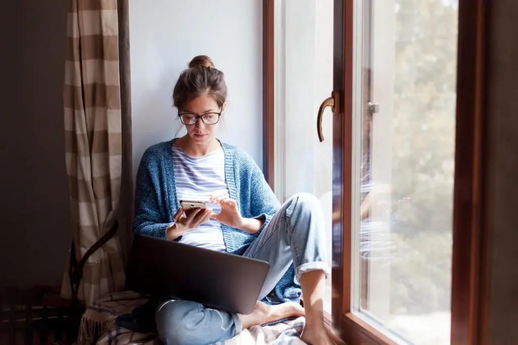 woman looking on her phone while sitting next to a sunny window