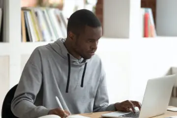 african american man in grey sweatshirt studying in a library