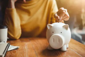 woman in yellow sweater putting a coin into a white piggy bank