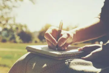 close up shot of a person writing in a notebook on a sunny day outside