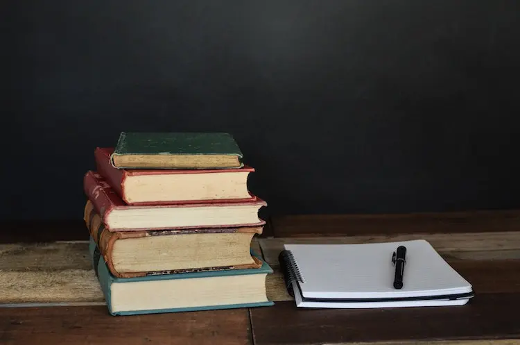 notebook with a pen next to a stack of old books