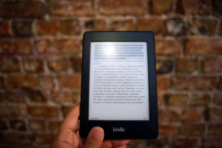 person holding a kindle book against a brick wall