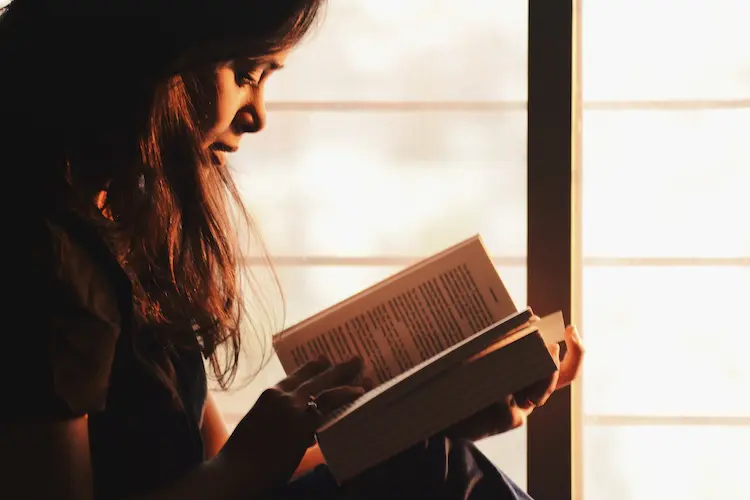 woman reading a book next to the window at sunset