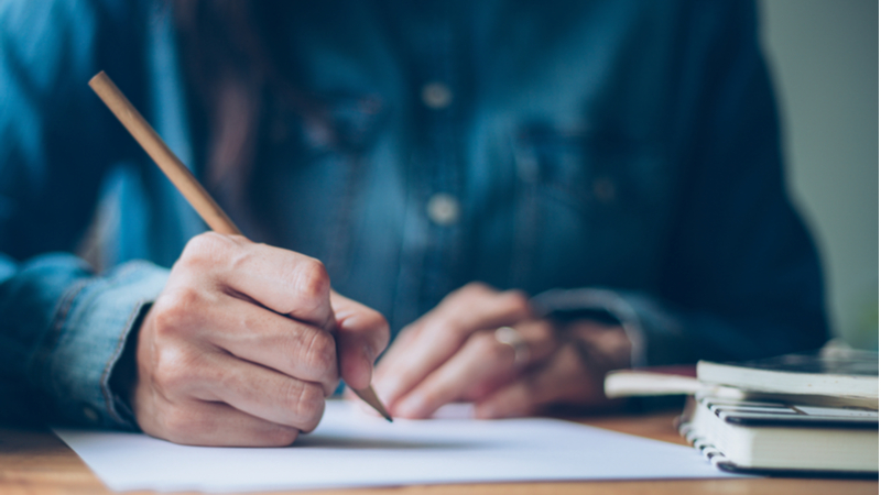 close up of a man holding a pencil and writing down notes