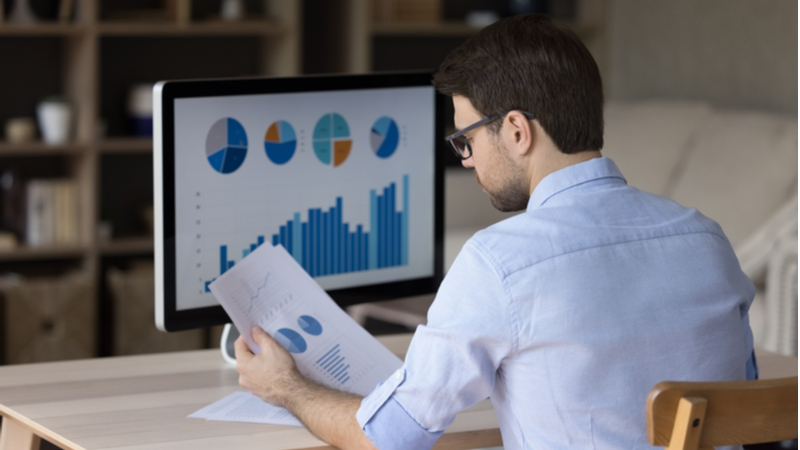 man in blue shirt looking at charts and comparing them to the computer