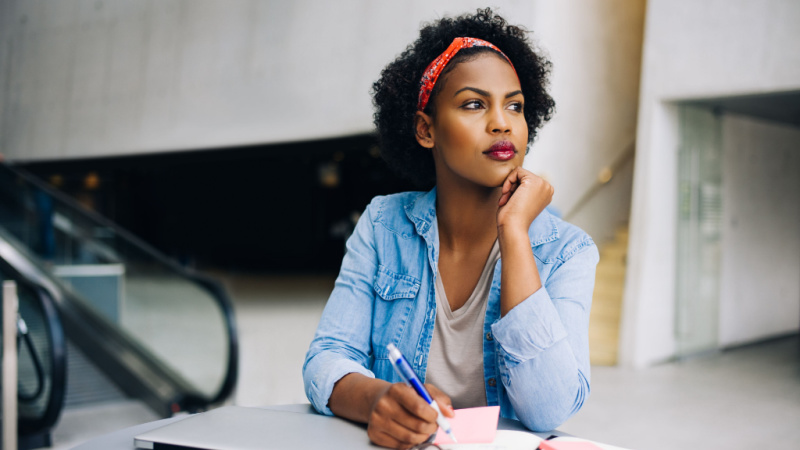 Focused young African woman thinking while taking notes